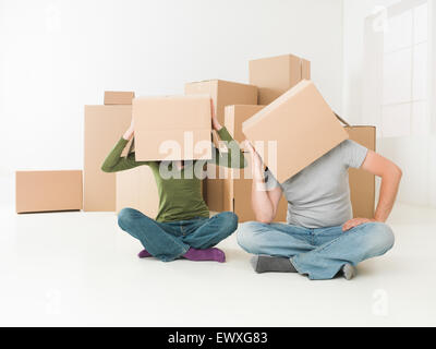 Giovane con scatole sulle loro teste seduto sul pavimento nella loro nuova casa, sensazione sottolineato Foto Stock