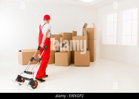 Deliveryman caucasici in rosso uniforme tenendo la mano carrello, ottenere pronto per caricare le scatole di cartone Foto Stock