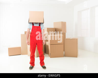 Vista frontale del deliveryman in piedi nella nuova casa con scatola che copre la sua testa. copia spazio disponibile Foto Stock