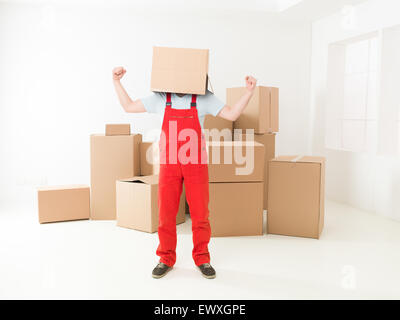 Deliveryman estatica tenendo le braccia, in piedi nella nuova casa con scatola che copre la sua testa Foto Stock