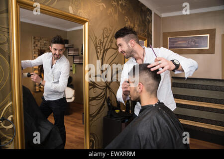 Bel giovane parrucchiere dando un nuovo taglio di capelli al cliente maschio a salottino Foto Stock