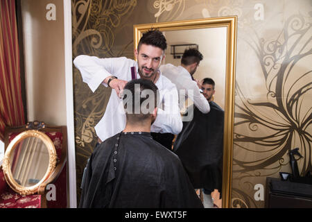 Bel giovane parrucchiere dando un nuovo taglio di capelli al cliente maschio a salottino Foto Stock