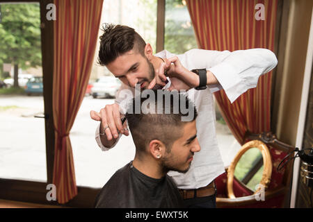 Bel giovane parrucchiere dando un nuovo taglio di capelli al cliente maschio a salottino Foto Stock