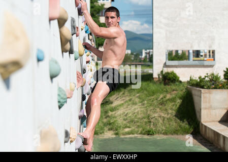 Giovane uomo si arrampica fino all'esterno di una parete di roccia - Egli è chiaramente determinato a fare la cima Foto Stock