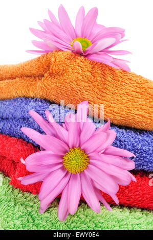 Primo piano di una pila di asciugamani di colori diversi e alcuni fiori di colore rosa su sfondo bianco Foto Stock