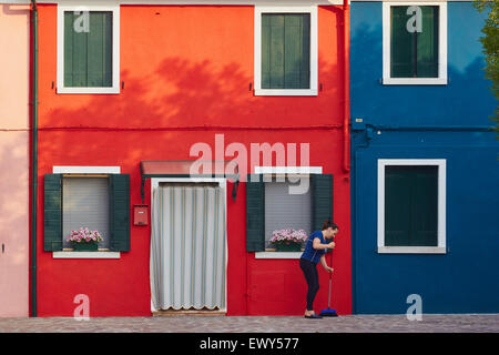 Donna spazzare davanti di colore rosso brillante casa di sunrise Burano Laguna di Venezia Veneto Italia Europa Foto Stock