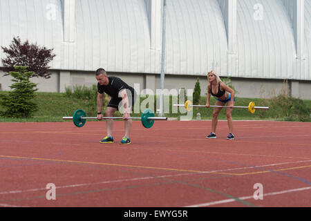 Un gruppo di giovani nella classe di Aerobica facendo un piegata Barbell Row esercizio Outdoor Foto Stock