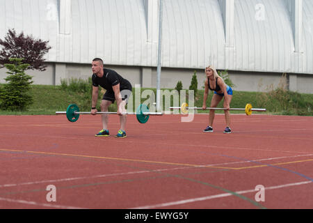 Un gruppo di giovani nella classe di Aerobica facendo un piegata Barbell Row esercizio Outdoor Foto Stock