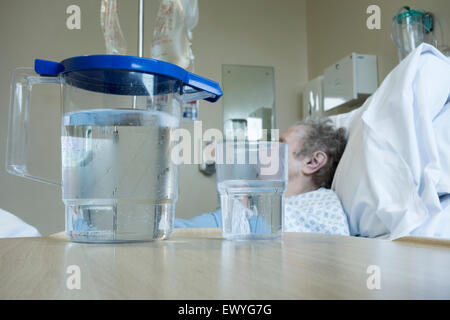 Signora anziana nel suo degli anni novanta nel letto di ospedale NHS ward con brocca di acqua sul comodino. Foto Stock
