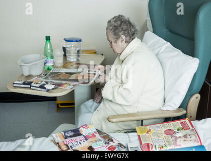 Signora anziana nel suo degli anni novanta la rivista di lettura sul NHS hospital Ward. Inghilterra, Regno Unito Foto Stock