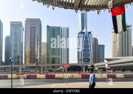 Uomo d'affari di Dubai a camminare sotto la bandiera degli Emirati arabi uniti di fronte al lago di Jumeirah Towers Foto Stock