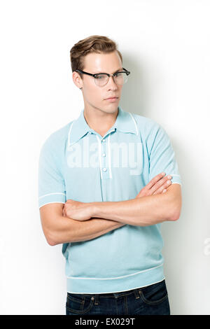 Un bel giovane uomo che indossa 50s occhiali e vintage top, ponendo bracci incrociati, guardando lontano Foto Stock