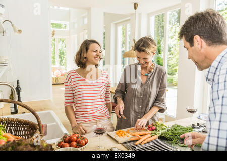 Tre adulti chattare mentre la preparazione di verdure fresche in cucina Foto Stock