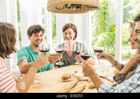 Cinque amici adulti facendo un toast al tavolo da pranzo Foto Stock