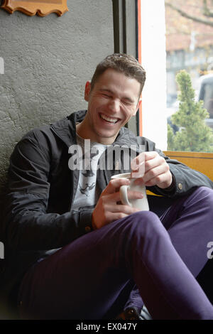 Giovane uomo seduto in cafe finestra ridere del sedile Foto Stock