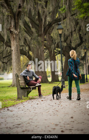 Un uomo su una panchina nel parco, donna cane a piedi a Savannah, Georgia, Stati Uniti d'America Foto Stock