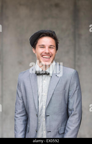 Giovane uomo che indossa il tappo piatto ed il filtro bow tie, ridendo Foto Stock