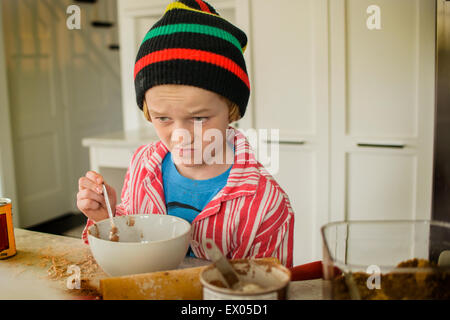 Ragazzo tirando la faccia mentre la miscelazione di torta in cucina Foto Stock