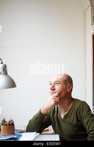 Uomo maturo alla scrivania con mano sul mento Foto Stock