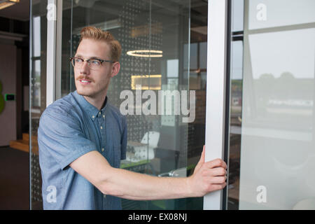 Giovane uomo guardando sopra la sua spalla da office porta Foto Stock