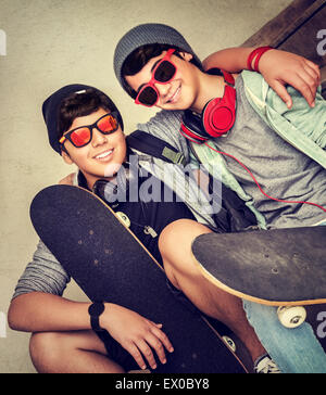Due lieti elegante teen boys seduta sul banco di lavoro e azienda di skateboard, allegro active amici godendo di sport all'aperto Foto Stock