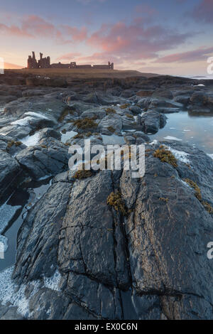 Il castello di Dunstanburgh shot dalla rocciosa foreshore al tramonto, Craster, Northumberland, Regno Unito Foto Stock