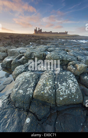 Il castello di Dunstanburgh shot dalla rocciosa foreshore al tramonto, Craster, Northumberland, Regno Unito Foto Stock