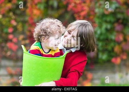 Felice di ridere il fratello e la sorella del bambino insieme giocando in giardino con una cesta per biancheria Foto Stock