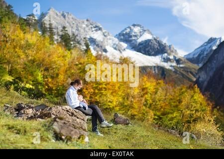 Giovani attiva madre allattare al seno il suo bambino neonato durante le escursioni nelle bellissime montagne coperte di neve in autunno Foto Stock