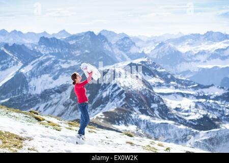 Giovane madre bella giocando con il suo neonato nella neve con belle montagne in background Foto Stock