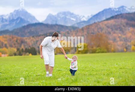 Giovane padre Felice a giocare con la sua bimba in un bellissimo campo tra montagne coperte di neve Foto Stock