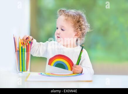 Dolce toddler funny girl dipinto un arcobaleno in una stanza bianca con una grande finestra in giardino Foto Stock