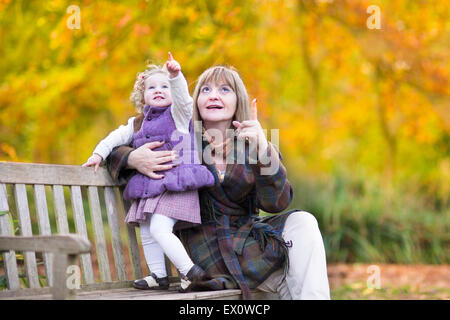 Bella Signora giocando con un po' di toddler girl su una panca di legno in un parco d'autunno con colorati alberi giallo Foto Stock