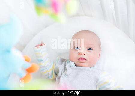 Carino piccolo neonato in un presepe bianco con giocattoli colorati Foto Stock