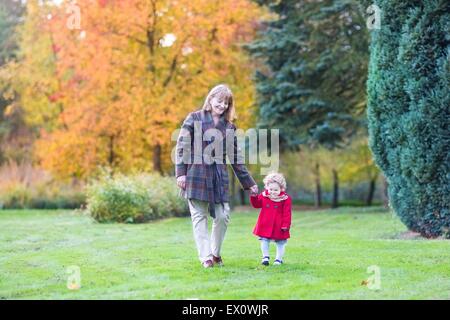 Bellissima ed elegante Donna che cammina con un simpatico bimbo ragazza in un parco di autunno Foto Stock