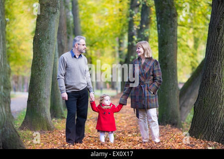 Felice di ridere giovane a camminare in un parco d'autunno con un bellissimo bimbo ragazza in un rivestimento di colore rosso Foto Stock