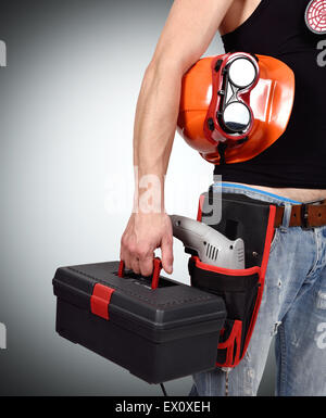 Lavoratore con toolbelt e casco contro uno sfondo grigio Foto Stock