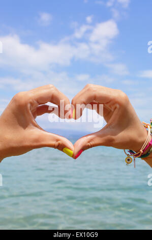 Forma di cuore facendo delle mani contro il mare e il cielo guardando l'acqua Foto Stock