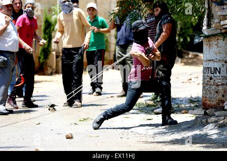 Kafr Qaddum, West Bank, Palestina. 03 Luglio, 2015. Una mascherata gioventù palestinese si prepara a scagliare una roccia a soldati israeliani che sono di stanza sulla strada principale del villaggio di Kafr Qaddum. Per la questione palestinese in Cisgiordania villaggio di Kafr Qaddum, gli abitanti del villaggio hanno celebrato il loro quinto anniversario delle marche contro i contenuti illegali insediamenti israeliani. Soldati israeliani assalto il villaggio, tenendo le posizioni in abitazioni civili e utilizzo di fuoco dei cecchini. In seguito, soldati israeliani spruzzata abbondante quantità di acqua chimica, noto come "skunk acqua" a manifestanti e a case, nonché utilizzando volleys di gas lacrimogeni da un Foto Stock