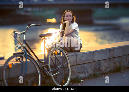 Ragazza con la bicicletta, seduto sul lungomare durante il tramonto. Processo trasversale film di stile. Foto Stock