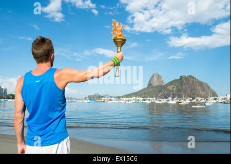 Giovane atleta maschio azienda torcia sport nei confronti di Rio de Janeiro in Brasile skyline con Sugarloaf Mountain in background Foto Stock