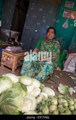 MYSORE, India - 04 novembre 2012: fornitore indiano si siede di fronte ad un mucchio di cavoli freschi nel mercato Devaraja. Foto Stock