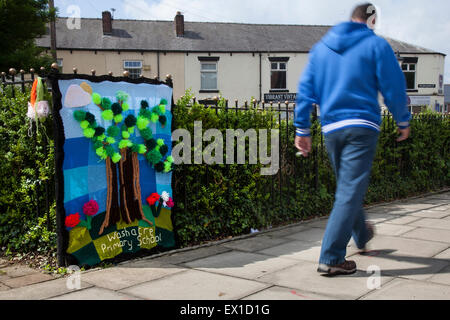 Westhoughton, Lancashire, Regno Unito 4 Luglio, 2015. Cernan Elias età 42, passeggiate passato la bomba di filato da 'Washacre scuola primaria" al filato Festival di bombardamenti, Westhoughton. Gruppo WCN, Rainbow mestieri, è portato a Dumfries in una festa di colori e di comunità e di intrattenimento. Da sempre giovani e vecchi, uomini e donne, esperti e il debuttante needlers coinvolto in a crochet, tessitura a maglia o a telaio piazze, lunghe strisce o rivestimenti a produrre arredamento di strada un impressionante e Curiose installazioni, il centro della città per un paio di giorni è inondato con colore. Cernan Elias/Alamy Live News Foto Stock