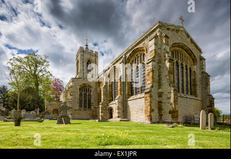 Basso angolo immagine di Castle Ashby chiesa nel Northamptonshire, Regno Unito, su una mattina di primavera con drammatica nuvole, cowslips e alberi Foto Stock