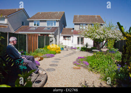 Un anziano gentiluomo si siede su una panchina per ammirare i fiori di primavera nel suo giardino, Somerset, Inghilterra, Regno Unito Foto Stock