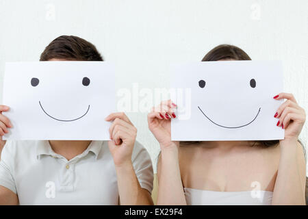 Coppia felice azienda smiley le loro facce mentre è seduto sul divano del soggiorno. Paio di coprire le loro facce di felice Foto Stock