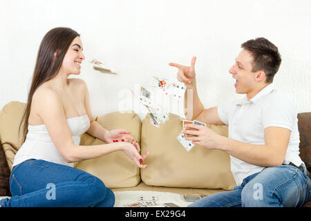Coppia sorridente gettando carte a ogni altro. Coppia giovane giocando a carte, sorridente e divertirsi stando seduti sul divano in soggiorno Foto Stock