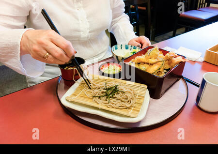 Donna più anziana che usa i bacchetti per mangiare soba e tempura. Primo piano di una mano invecchiata che tiene i bacchetti. Foto Stock