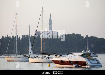 Barche a vela ancorate nel mare Adriatico vicino al litorale con una vista della Santa Eufemia torre campanaria al tramonto a Rovigno Croazia Foto Stock