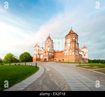 Alberi verdi e gras e cielo blu a giornata di sole. Stone Road al bellissimo Castello di Mir in Bielorussia. Fortilizio medievale divenne la vista per a Foto Stock